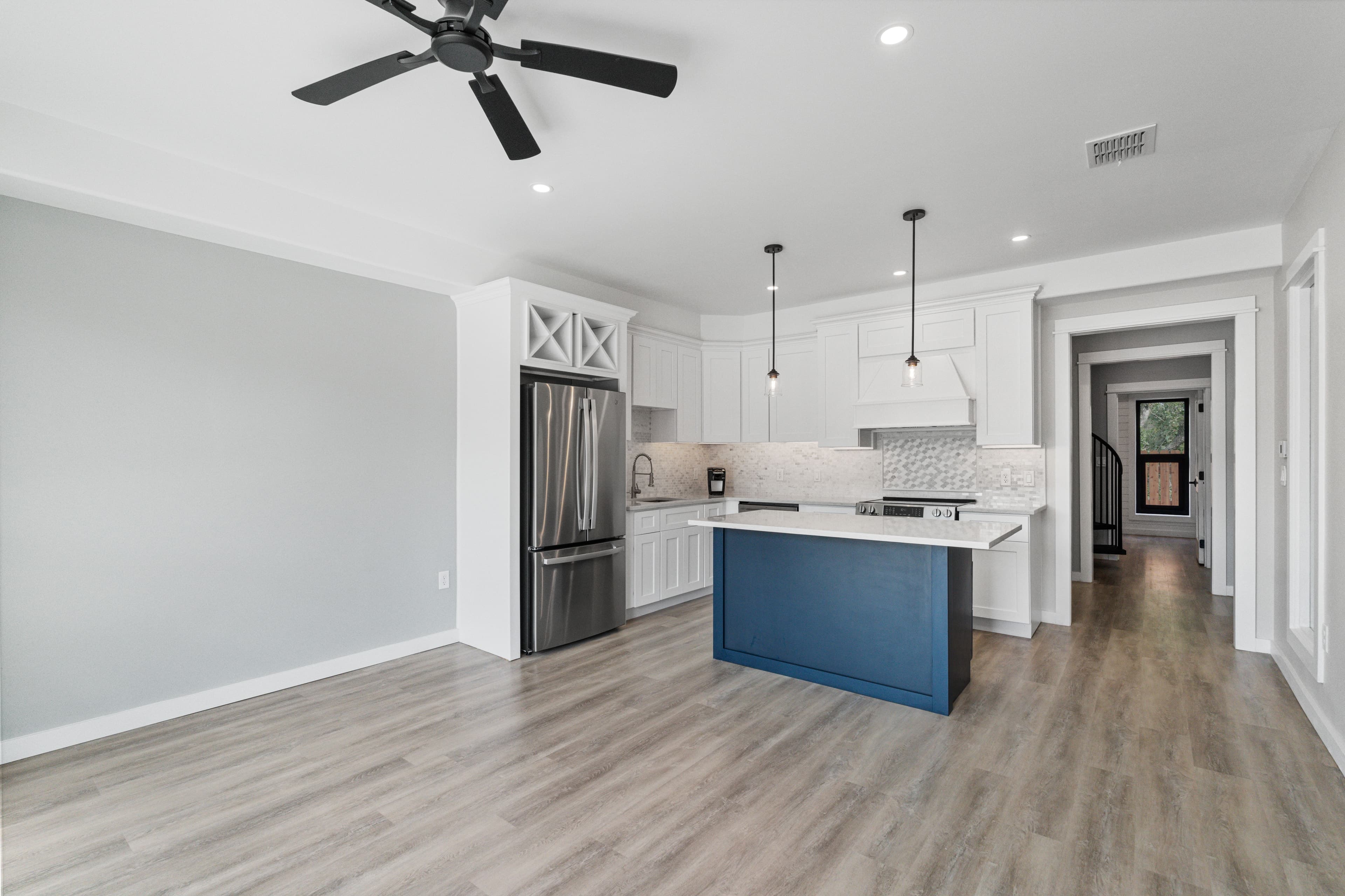 Kitchen with a blue island and white cabinets, looking down the hall